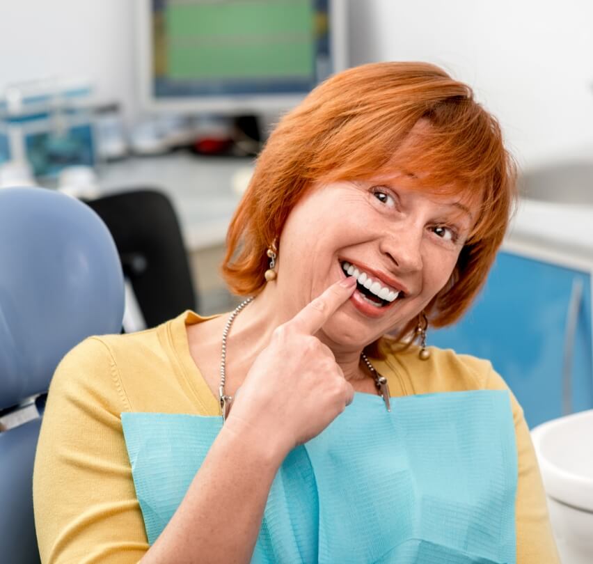 Woman pointing to smile after tooth replacement with dental implants
