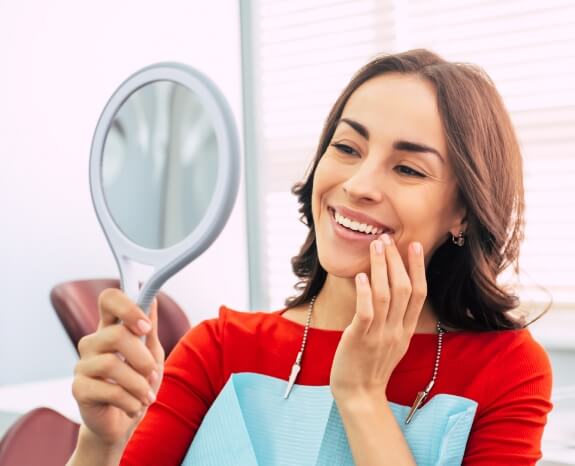 Woman looking at smile after tooth replacement with dental implants