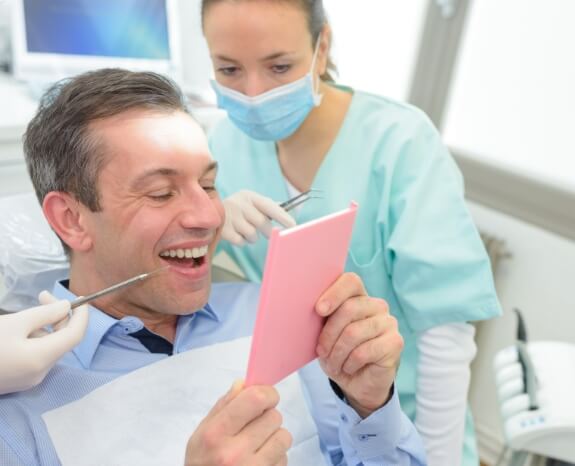 Man with dental bridge looking at smile in mirror