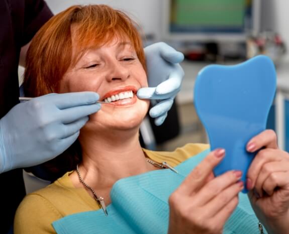 Woman looking at smile after tooth replacement with dental implants