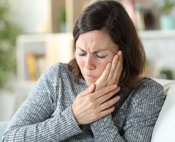 Woman holding cheek in pain before T M J therapy